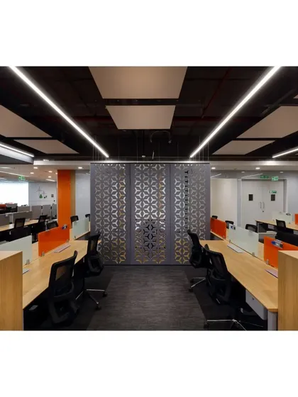 An aisle view of the office floor, showcasing the linear arrangement of workstations and the use of decorative, laser-cut screens as functional dividers. The overhead linear lighting reinforces the sense of direction and flow.