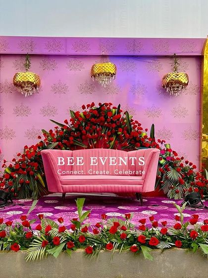 A closer look at the pink and red rose-themed reception stage. The dense arrangement of red roses around the seating area creates a powerful focal point, complemented by the soft pink backdrop and golden accents.