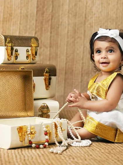 A 10-month-old baby girl in a traditional South Indian style Kasavu dress, playing with pearl necklaces.