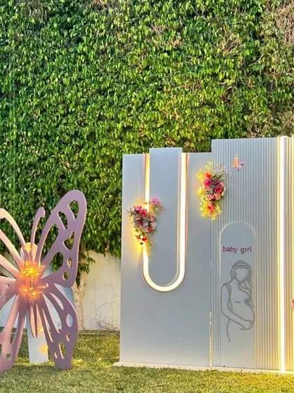 A modern and chic photo backdrop for a baby girl's welcome party, with clean lines, integrated lighting, and a large butterfly prop.