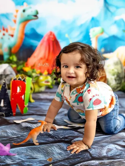 Crawling through the Jurassic jungle! This little one's sweet smile and curly hair are just adorable against the colourful dinosaur backdrop.