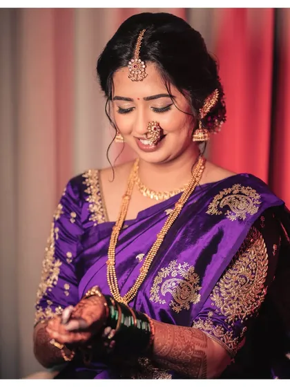 Akshaya on her wedding day, with a muted makeup look that allows her unique purple saree and traditional jewelry to take center stage.