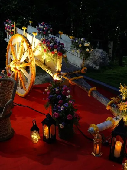 This unique wedding decor piece features a rustic bullock cart adorned with beautiful flower arrangements and surrounded by warm lanterns, creating a magical and picturesque setting for an evening celebration.