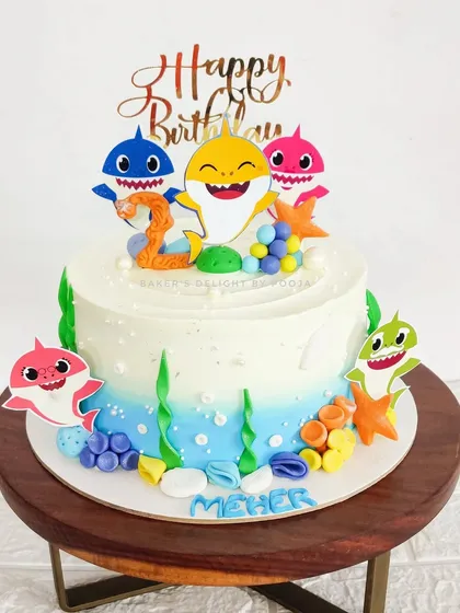 Baby Shark, doo doo doo! This fun and colorful cake brings the underwater world of Baby Shark to life with an ombre blue whipped cream finish, edible seaweed, and the whole shark family.