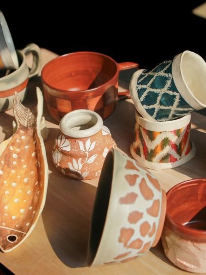A vibrant and eclectic mix of student pieces, from a fish shaped platter to cups with intricate, hand painted patterns.