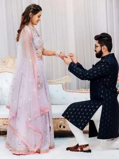 The groom puts a ring on his bride's finger, a classic engagement moment.