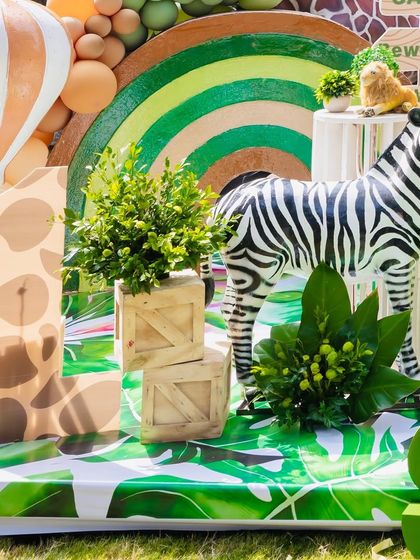 A close-up of the "Wild One" safari decor for Shourya's first birthday. This shot highlights the number '1' prop with a giraffe pattern and a zebra figure among green plants.