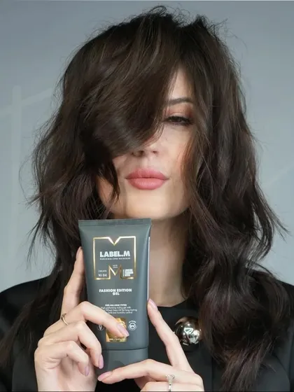 The model presents the 'VELAIR' look while holding the Label.M Fashion Edition Wax Spray used to achieve the style. This highlights the soft, tousled finish and fluid textures that define this contemporary cut.