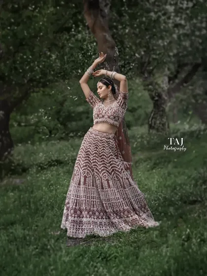 A graceful and artistic bridal portrait in a lush, green setting. The bride's pose is elegant and expressive, like a dancer in nature.