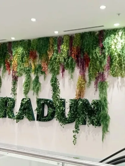 A large-scale artificial greenery installation in a commercial building, featuring hanging plants and 3D lettering. This project in Dehradun creates a massive, cascading green feature wall.