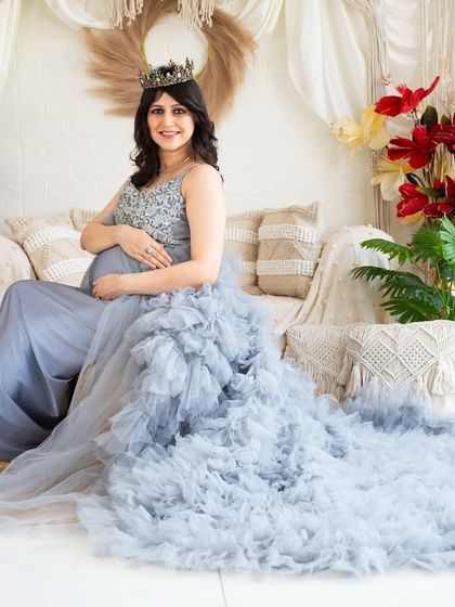 A serene and royal portrait. The mother-to-be is seated comfortably on our studio couch, wearing a light blue gown with a magnificent ruffled train that cascades across the floor.