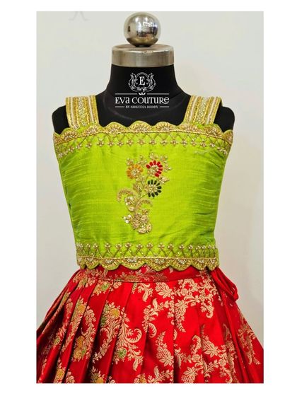 A detailed view of a sleeveless lime green blouse. The scalloped border and floral motif are created with careful hand embroidery.
