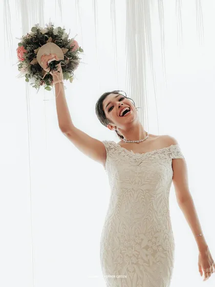 A moment of pure elation as the bride raises her bouquet in the air with a joyful laugh.