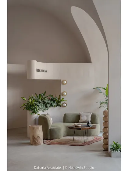A close-up of a cozy nook designated as a waiting area. The organic shape of the green sofa is complemented by the built-in planter and the soft glow of the wall-mounted lights.