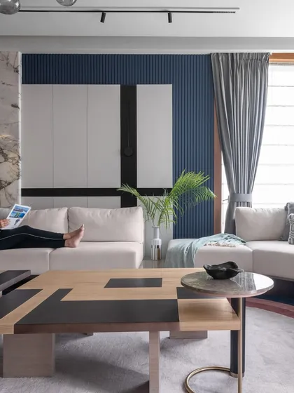 This shot captures the geometric patterns of the coffee table against the bold blue fluted wall. Every element, from the furniture shape to the color palette, contributes to the room's modern and luxurious vibe.