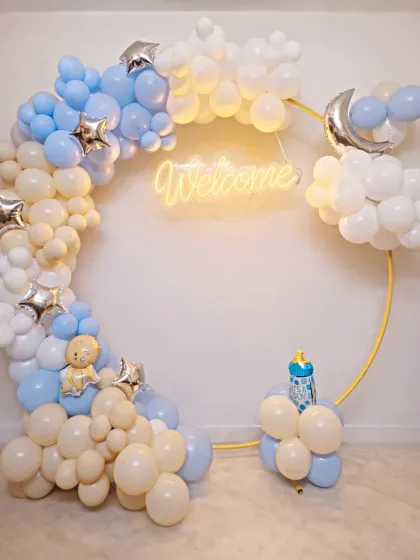This 'A Sky Full of Stars' theme is perfect for a magical welcome home. We used a modern circular gold frame adorned with a cloud-like balloon garland in pastel blue, white, and cream, complete with a glowing 'Welcome' neon sign and silver moon and star accents.