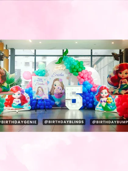A full stage setup for a Little Mermaid fifth birthday, featuring multiple character cutouts and a light-up number '5'. The balloon colors perfectly match Ariel's world.