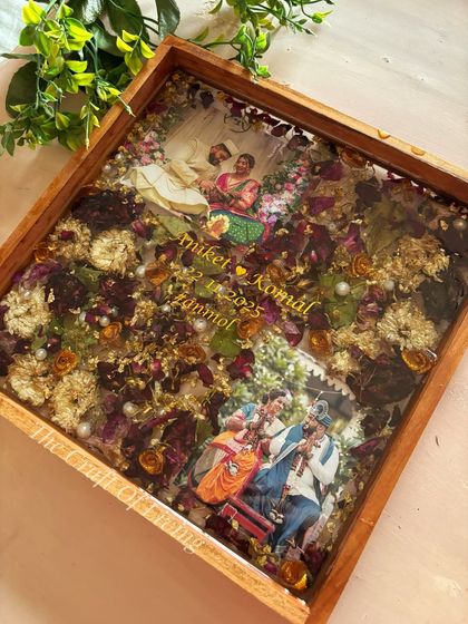 An angled view of the dual-photo wooden frame, showing the glossy finish of the resin and how the light catches the gold flakes and pearls scattered among the flowers.