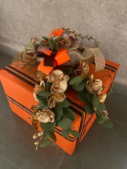 A close-up of our vibrant orange gift box, showcasing the detailed golden foliage and multi-textured bow. This highlights the craftsmanship that goes into our signature gift wrapping.