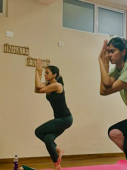 Two students holding Garudasana (Eagle Pose), a standing balance that improves focus and opens the shoulder and hip joints.