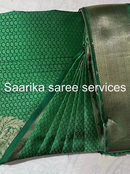 A beautiful green brocade saree with a silver border. The pleats are set to showcase the rich texture of the fabric.