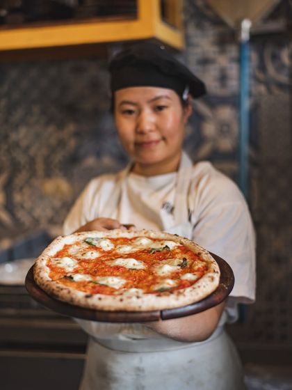 Fresh from the oven and ready to serve. One of our chefs proudly presents a classic Margherita pizza, showcasing the beautiful char and melted cheese.