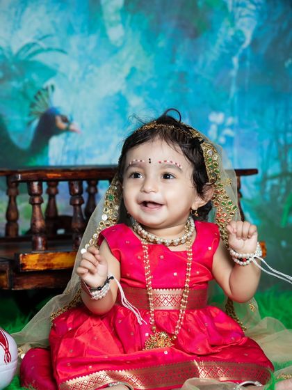 A beautiful baby girl dressed as Radha, with a sweet smile and traditional jewelry.