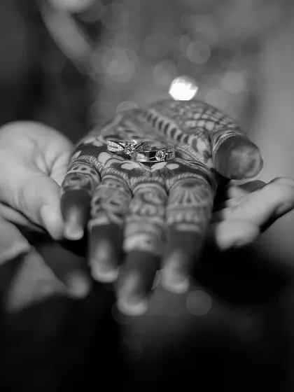 A symbolic black and white photo showing the engagement rings resting in the groom's hand over the bride's henna. It's a beautiful, artistic detail shot.