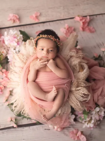 This little doll is wide awake and surrounded by soft pink blossoms. The floral elements perfectly complement her delicate features and pink swaddle.