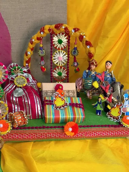 A beautiful Lohri hamper featuring a decorated arch and traditional dolls. The vibrant colors of the gift wrapping and gota patti work perfectly capture the joyous mood of the festival.