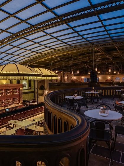 A view from the mezzanine level, looking down across the main floor towards the bar. This shot captures the grandeur of the glass canopy ceiling and the sweeping curves of the balcony, key elements in the architectural storytelling.