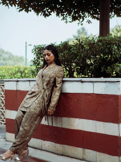A full-body shot of Anasuya Sengupta leaning against a striped wall. The composition uses strong lines and a relaxed pose to create a stylish image.