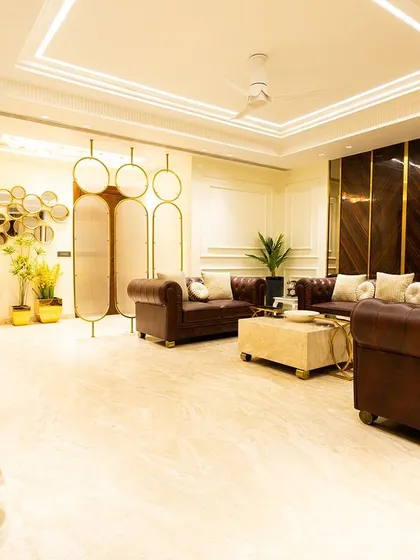 A spacious and bright living room featuring classic leather sofas and modern gold accents. The decorative screen and strategically placed plants add layers of texture and interest.