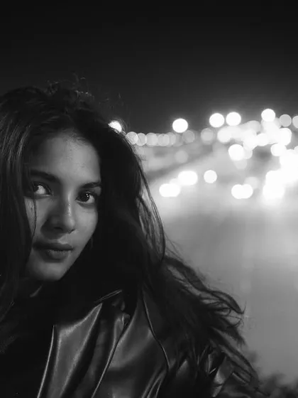 A striking black and white night portrait of a woman looking directly at the camera, with the blurred lights of a highway stretching out behind her. This shot exemplifies my raw, urban cinematic style.