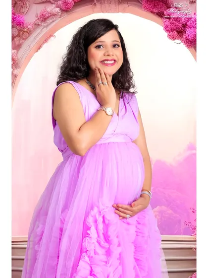 A bright and happy studio portrait using a pink floral archway. The vibrant colors and cheerful smile make this a beautiful celebration of the joy of pregnancy.