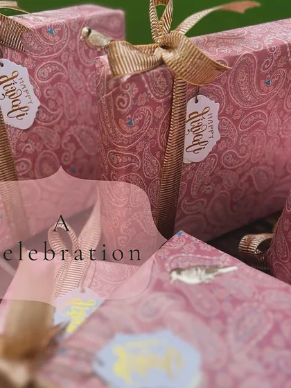 The packaging for the "Jashn" collection. These pink paisley-patterned boxes are tied with gold ribbons and adorned with a small bird motif, embracing traditional Indian design in a modern context.