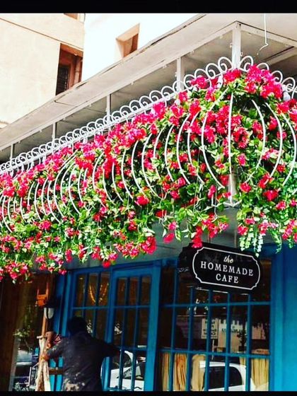 I help make storefronts stand out. For this cafe, I created a beautiful overhead entrance decoration using a white metal frame filled with bright pink artificial bougainvillea. This kind of exterior decor is great for attracting customers to cafes, boutiques, and restaurants.