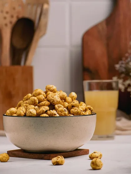 A bowl of roasted snacks paired with a glass of juice in a bright kitchen scene. This pairing suggests a perfect evening snack combination to the customer.