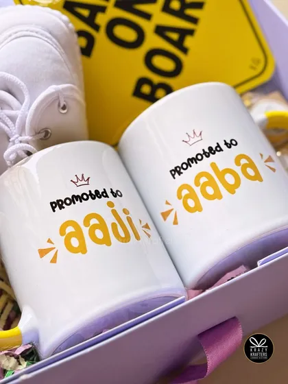 A close-up on the 'Promoted to Aaji & Aaba' mugs. The cheerful font and crown detail make the message feel celebratory.