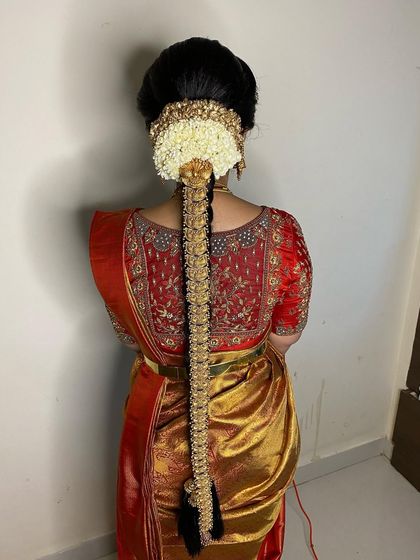 A classic muhurtham hairstyle with a long braid, temple jewellery, and a full arrangement of fresh jasmine flowers, paired with a red and gold silk saree.
