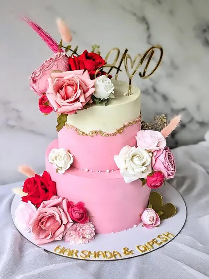 A beautiful two-tier cake for a Roka ceremony. The design combines a soft pink lower tier with a white upper tier, separated by a delicate gold fault line and adorned with a mix of red, pink, and white roses.