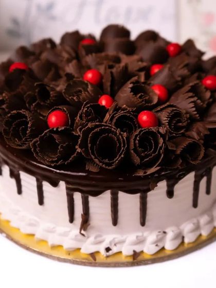 A classic Black Forest cake with chocolate shavings, chocolate drip, and bright red cherries.