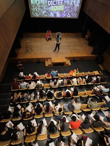 An overhead shot of the packed auditorium during "La Dictée pour Tous." The scale of participation shows the enthusiasm for French language learning in our community.