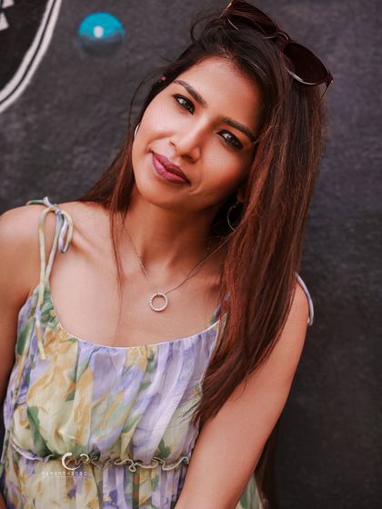 A calm and serene portrait against a dark, textured wall. Her gentle smile and direct gaze create a moment of quiet connection.