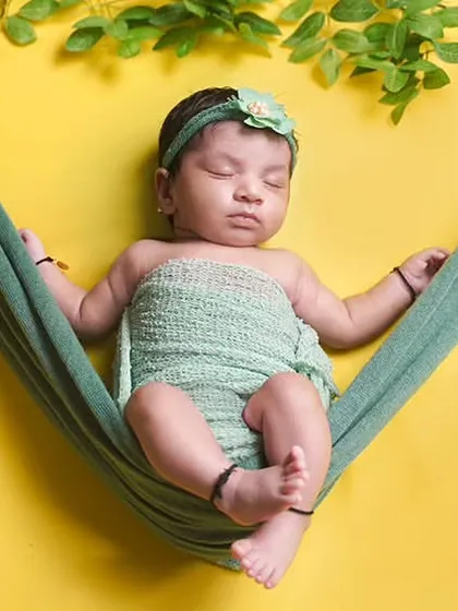 A newborn relaxes in a green hammock against a bright yellow backdrop, all set up in the family's living room.