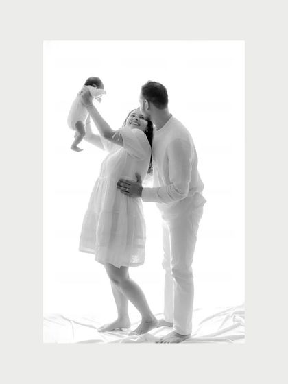 A moment of pure joy as the mother lifts her newborn into the air while the father looks on lovingly. This black and white image captures the dynamic happiness of a new family.