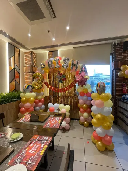 A colorful and fun decoration for a 3rd birthday party. This setup features balloon pillars in pastel shades, a golden shimmer backdrop, and foil balloons spelling out the birthday girl's name.
