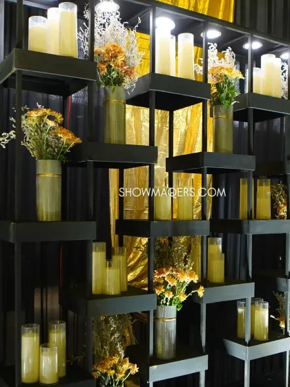 A modern shelving unit used as a decor piece, filled with candles and small floral arrangements to complement the black and gold theme.