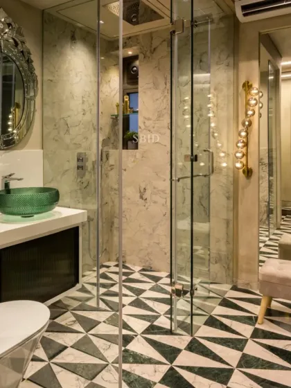 This master bathroom features a stunning geometric floor made of green and white marble, a floating vanity with a green glass basin, and a large Venetian mirror. The glass shower enclosure keeps the space feeling open and bright.
