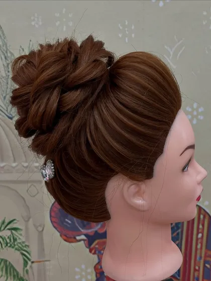 A high bun with braided details, beautifully executed by a student on a mannequin head. Practice is key to perfection.